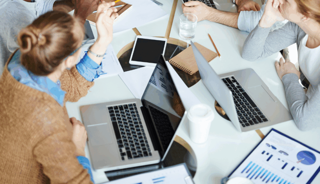 Equipa em reunião com computadores e relatórios, ilustrando diagnóstico e planeamento das necessidades de formação e competências na empresa